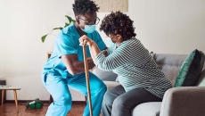 A care worker helps a woman up from her chair
