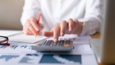 Person's hands operate calculator while writing on pad of paper