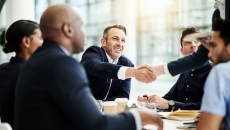 People shake hands over a conference room table