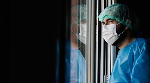 Person in PPE stares through a window