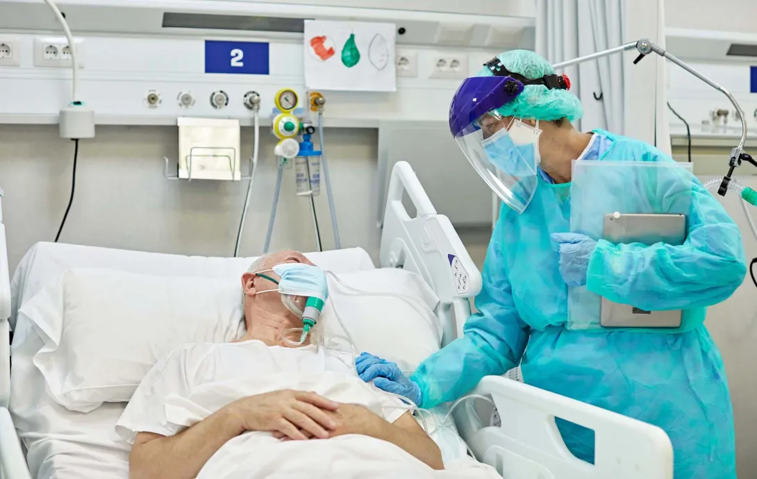 Person in PPE stands by person in hospital bed