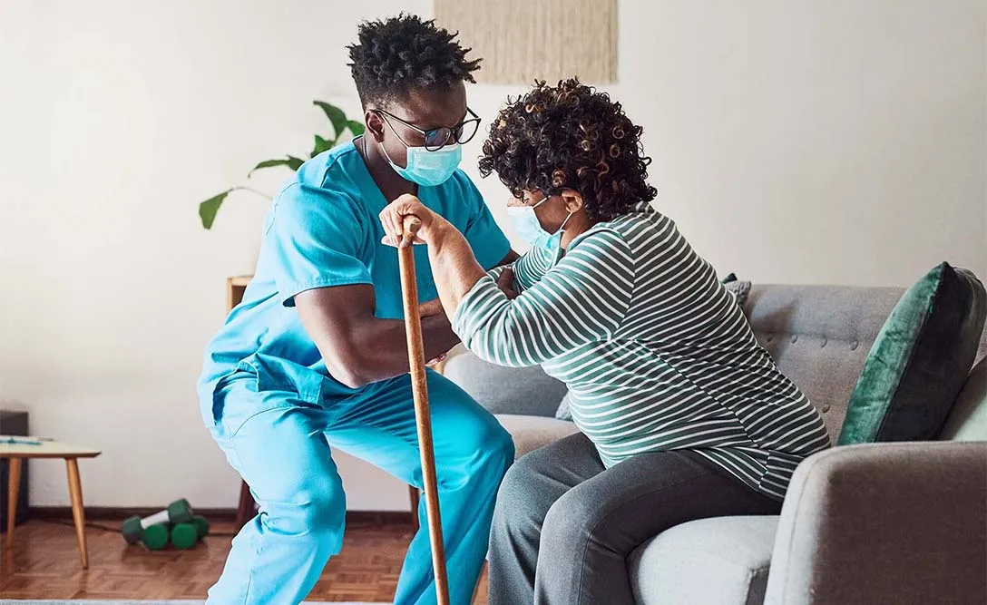 A care worker helps a woman up from her chair