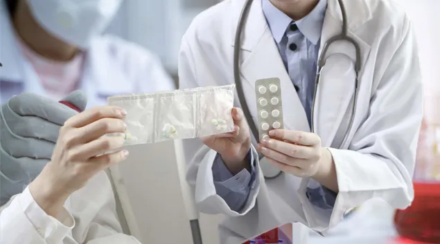 Two people in lab coats examine a pill pack.
