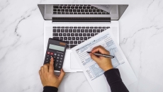 Hands at a calculator and laptop with tax form