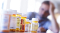 Person at table with many prescription pill bottles