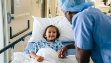Adult by hospital bed holds child's hand