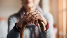 Person sitting with hands on a cane