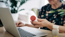 Person holding perscription bottle and using laptop