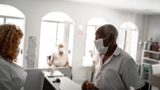 People in masks at desk of clinic. Photo: FGTrade/Getty Images