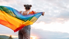 Person with rainbow flag watches sunset