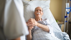 Healthcare professional holds patient's hands at hospital bed