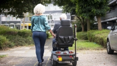 Person walking next to another using mobility scooter