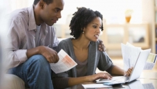 Couple on couch with bills at computer on coffee table