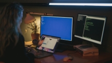 Person working at laptop with dual monitors showing computer code