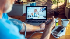 Patient using blood pressure cuff while talking to doctor on laptop screen