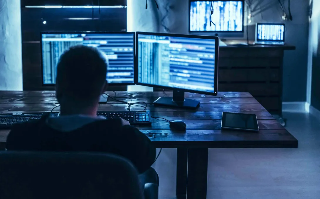 Person in dark room in front of computer monitors Person in dark room in front of computer monitors