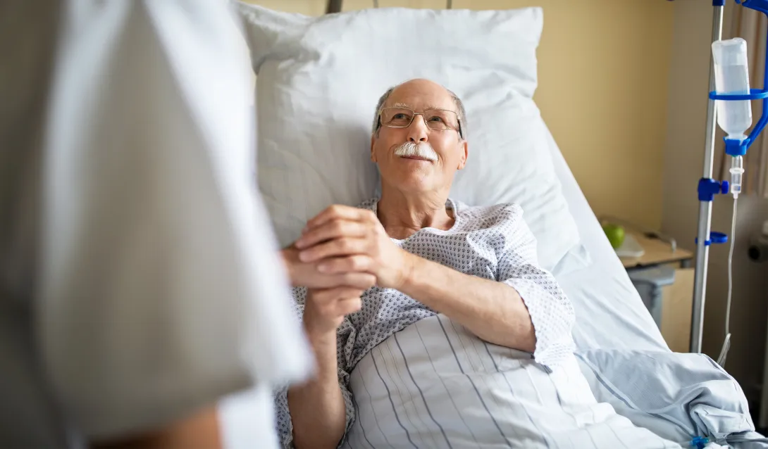 Healthcare professional holds patient's hands at hospital bed Healthcare professional holds patient's hands at hospital bed