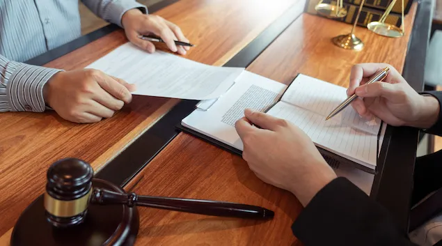 Person with gavel writing in book with someone at desk