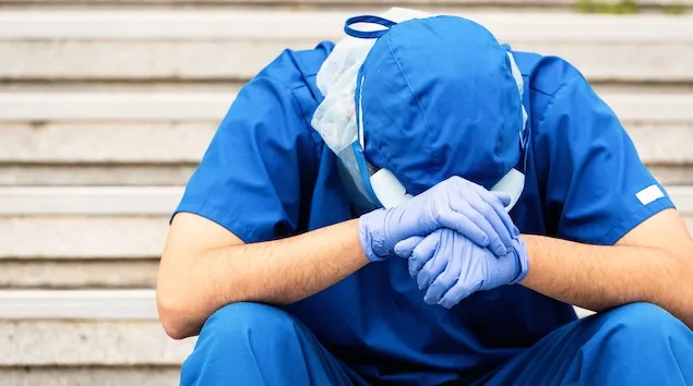 Person in scrubs holding head while seated