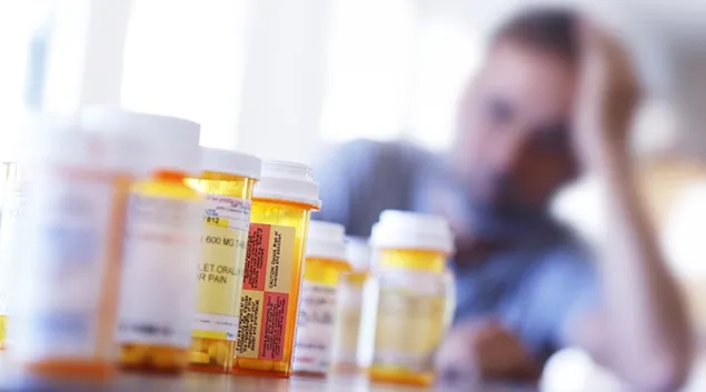 Person at table with many prescription pill bottles