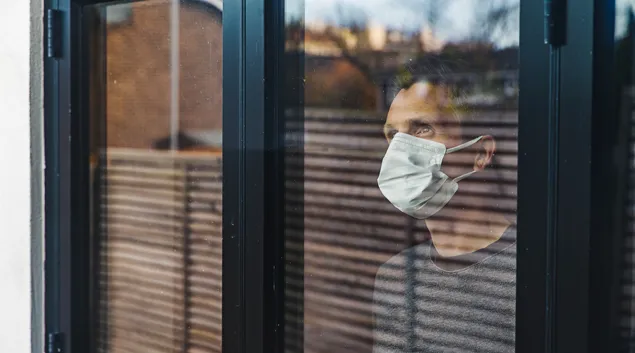 Person in mask stares through a window