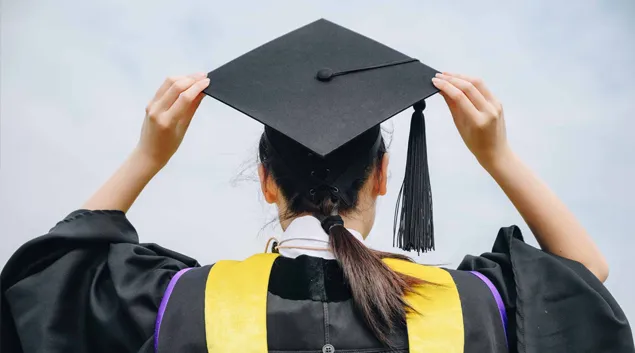 Graduate in robes holding cap Graduate in robes holding cap