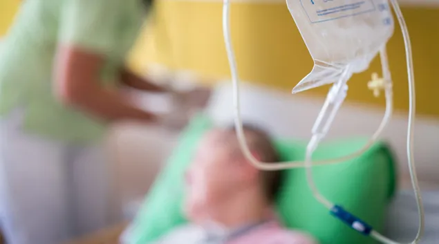 Person in hospital bed with staffer standing nearby