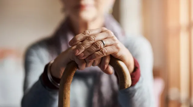 Person sitting with hands on a cane