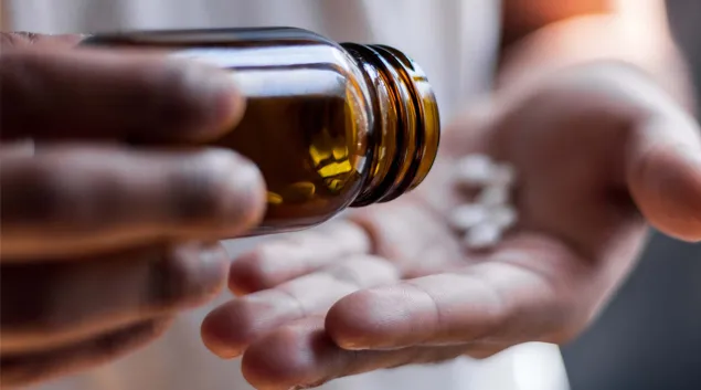 Hands tapping pills out of a pill bottle