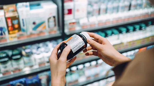 Hands holding a supplement bottle in a pharmacy