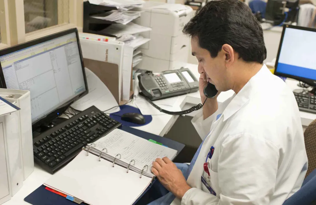 Doctor on telephone in front of book and screens