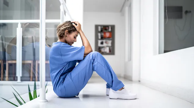 Healthcare worker sitting on the floor of a facility with their head in their hands