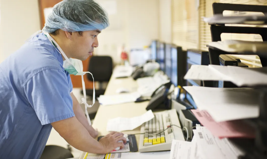 Medical professional at computer with papers on desk. Photo: Helen King/Getty Images