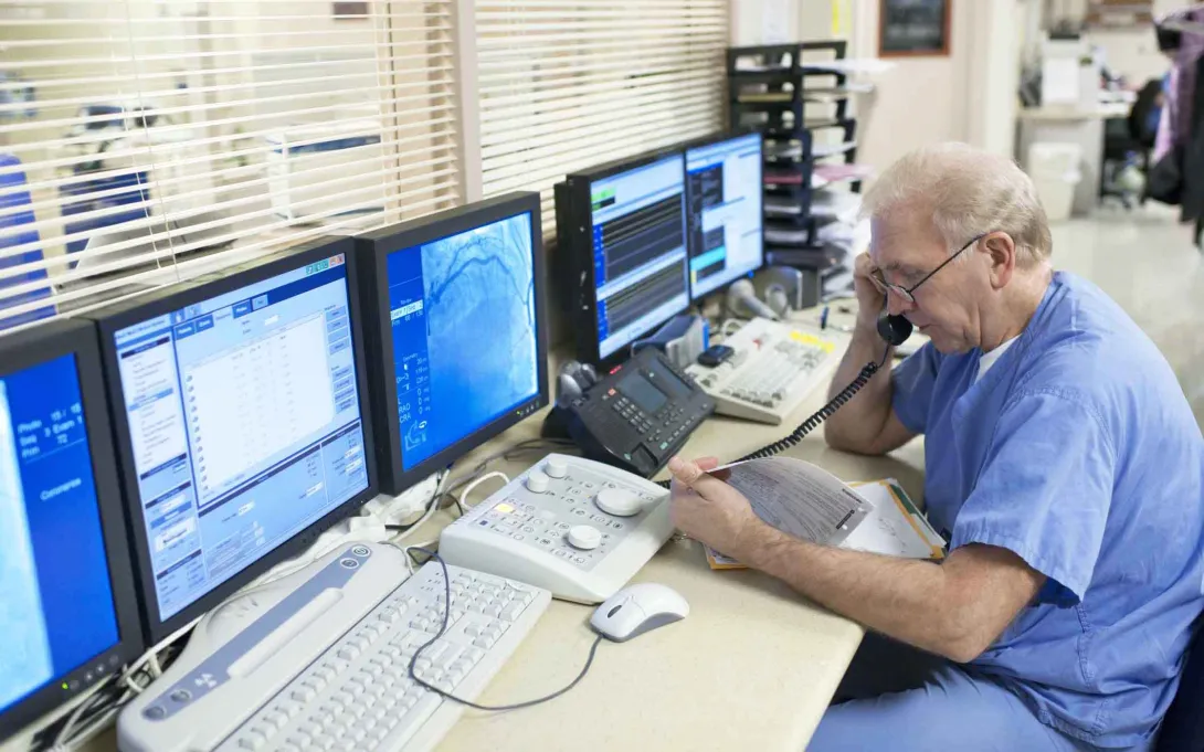 Doctor on phone in front of multiple computer screens