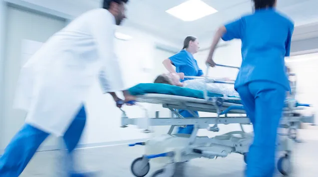 Healthcare providers rushing a hospital bed with a patient in it through a hall