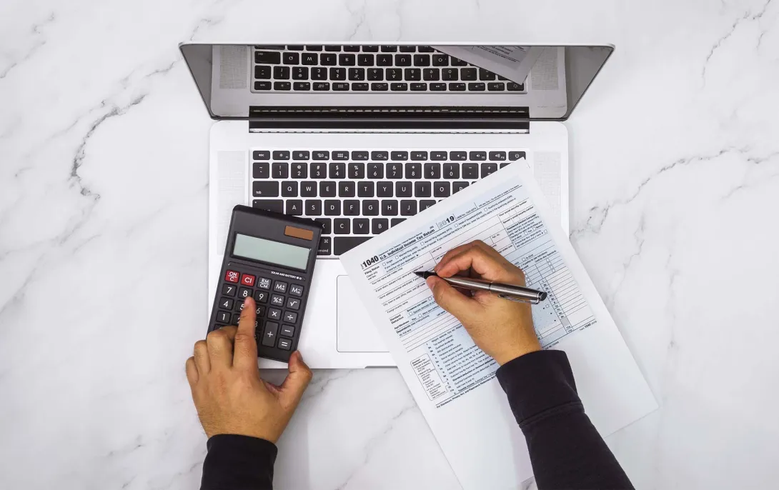 Hands at a calculator and laptop with tax form