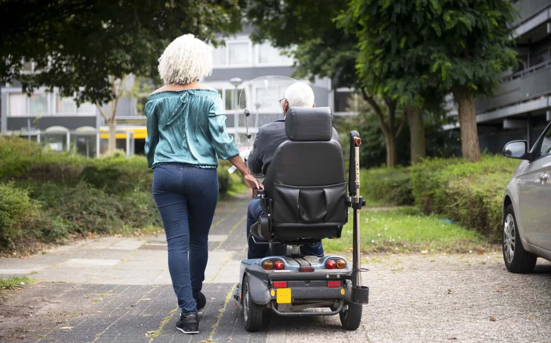 Person walking next to another using mobility scooter