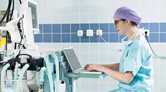 Health professional with a laptop in front of medical monitor