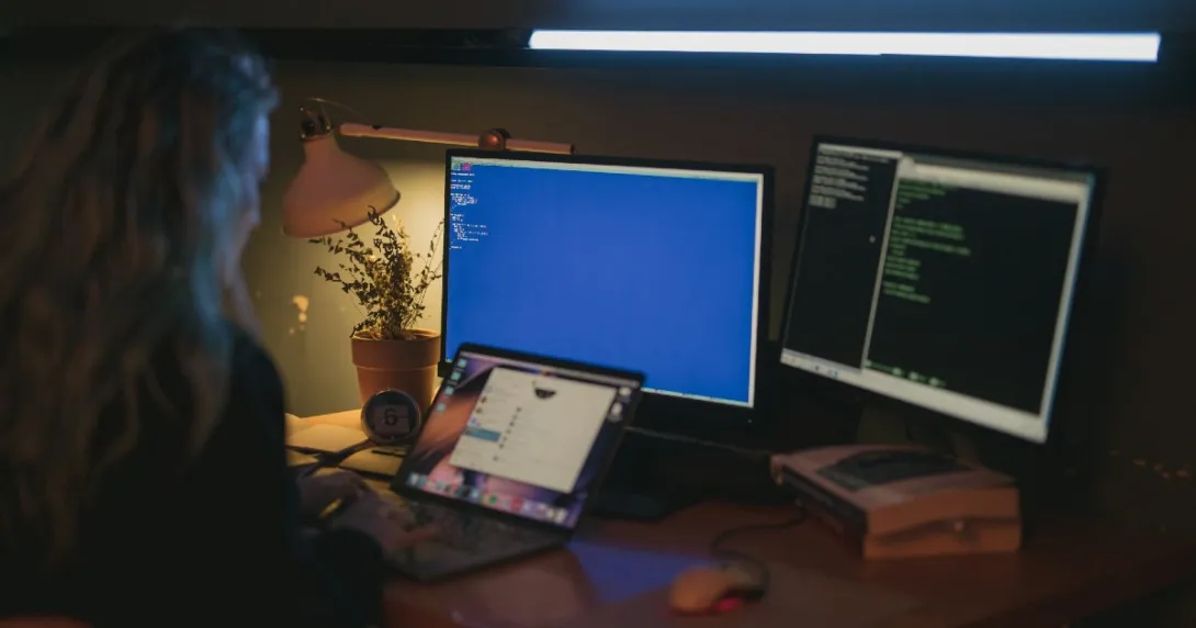 Person working at laptop with dual monitors showing computer code