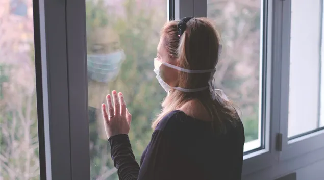 Person in mask stares out window