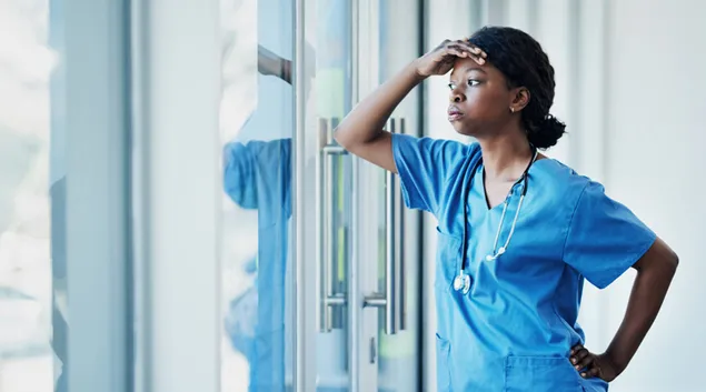 Person in scrubs leans at window
